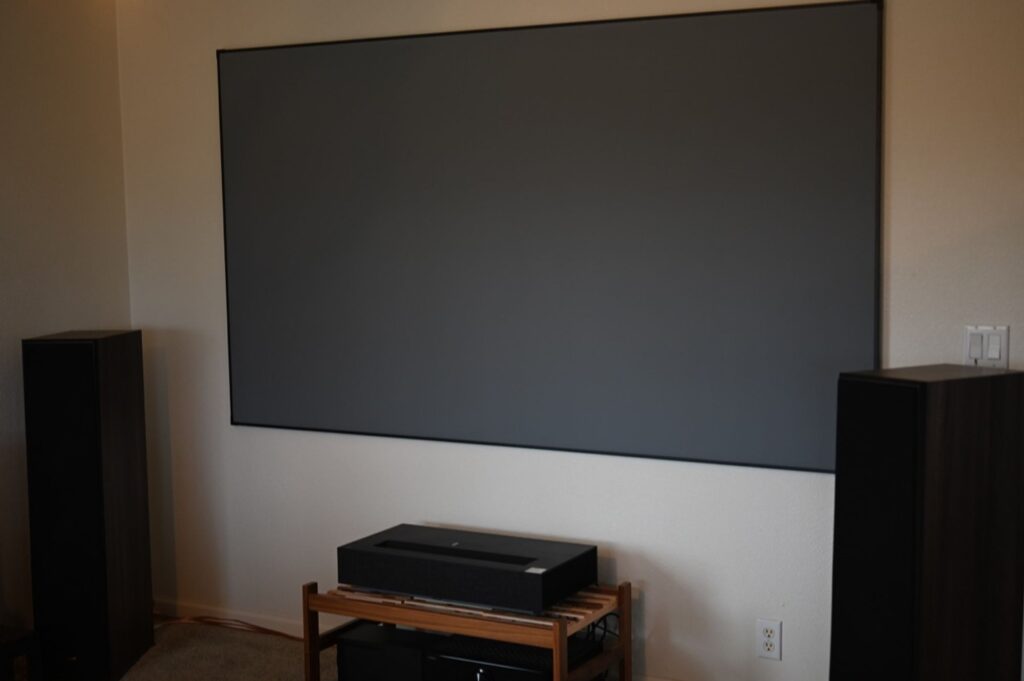 The LG CineBeam HU915QB UST projector sits underneath a screen, ready to project onto it.